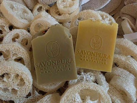 Set Naturseife-Lavendel Traubenkern Zwei Seifenstücke mit Etiketten auf einer weichen Unterlage und herzförmiger Holzschale.